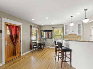 Kitchen with dark stone counters, decorative light fixtures, a breakfast bar area, backsplash, and glass insert cabinets