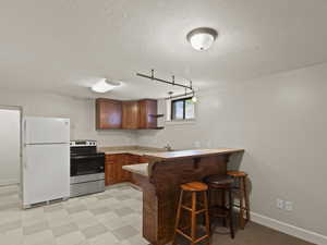 Kitchen featuring freestanding refrigerator, a peninsula, stainless steel range with electric cooktop, a breakfast bar, and light countertops