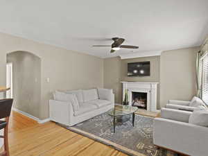 Living area featuring arched walkways, light wood floors, a ceiling fan, and a tiled fireplace