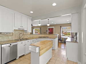 Kitchen with white cabinets, stainless steel dishwasher, light stone counters, and recessed lighting