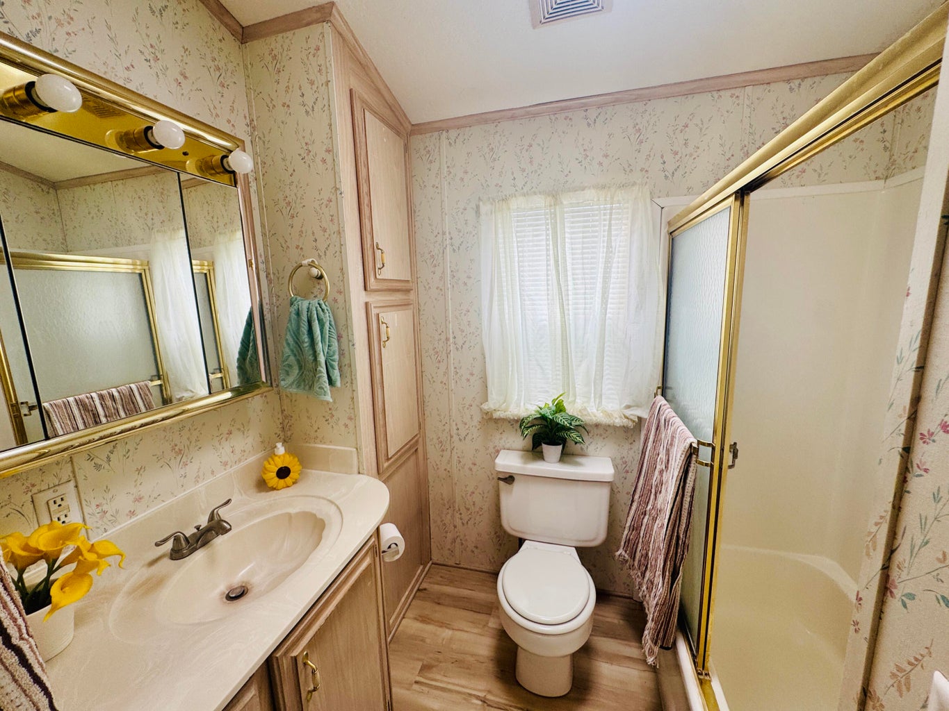 Bathroom with wallpapered walls, a shower stall, light wood-style floors, and vanity