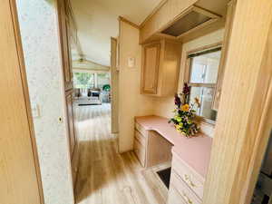 Hall with light wood finished floors, lofted ceiling, an office area, and wallpapered walls
