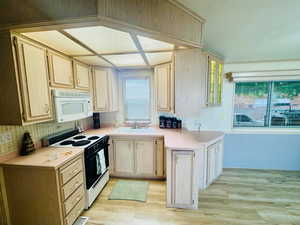 Kitchen with light brown cabinets, range with electric stovetop, white microwave, light countertops, and light wood-type flooring