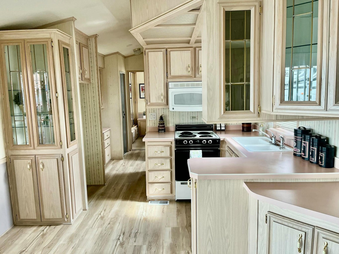 Kitchen with range with electric stovetop, light countertops, light wood finished floors, white microwave, and light brown cabinetry