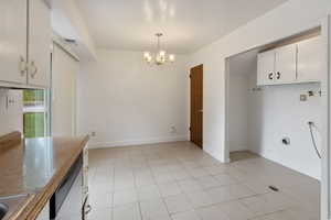 Kitchen with a chandelier, hanging light fixtures, light tile patterned floors, white cabinets, and dishwasher