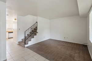 Unfurnished living room featuring light colored carpet, light tile patterned floors, and stairs