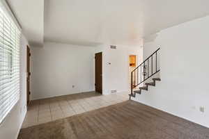 Unfurnished living room with light tile patterned flooring, stairway, and light carpet