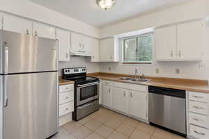 Kitchen featuring appliances with stainless steel finishes, light tile patterned floors, white cabinets, under cabinet range hood, and light countertops