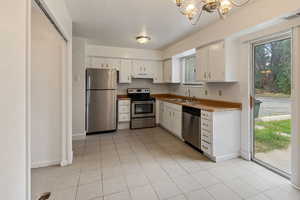 Kitchen with stainless steel appliances, a chandelier, light tile patterned floors, white cabinetry, and under cabinet range hood