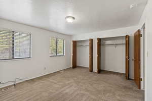 Unfurnished bedroom with two closets, light carpet, and a textured ceiling