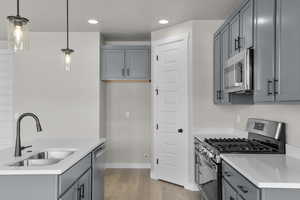 Kitchen featuring gray cabinetry, appliances with stainless steel finishes, light wood finished floors, hanging light fixtures, and recessed lighting