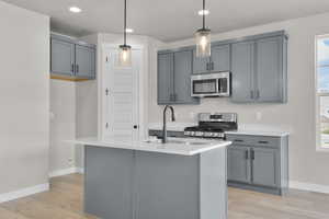 Kitchen featuring gray cabinetry, stainless steel appliances, hanging light fixtures, light wood-style flooring, and recessed lighting