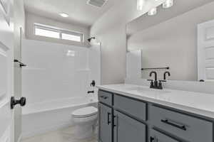 Full bath with  shower combination, vanity, a textured ceiling, and light marble finish floors