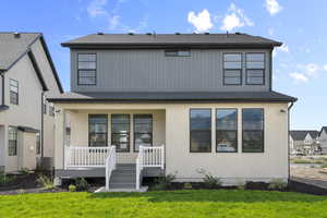 Rear view of property with a lawn, a shingled roof, covered porch, and stucco siding
