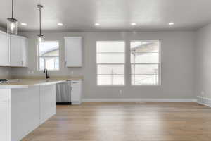 Kitchen featuring white cabinets, pendant lighting, light wood-style flooring, a textured ceiling, and stainless steel dishwasher
