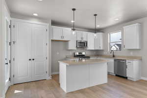 Kitchen with light countertops, white cabinetry, stainless steel appliances, hanging light fixtures, and recessed lighting
