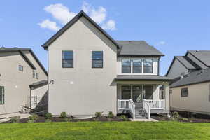Back of property featuring a lawn, covered porch, stucco siding, and roof with shingles