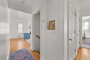 Hallway featuring ornamental molding and hardwood  floors off living area entrance to main bath and an upstairs landing with stairs down to the lower level.