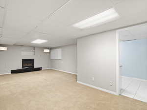 Finished basement featuring a drop ceiling, light carpet, and a tile fireplace