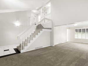 Unfurnished living room featuring high vaulted ceiling, carpet flooring, tile patterned flooring, and stairway