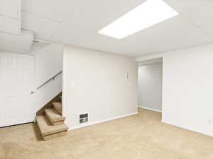 Finished below grade area featuring light carpet, a paneled ceiling, and stairway