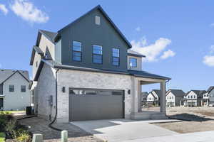 View of front of house with an attached garage, driveway, a residential view, stone siding, and a porch