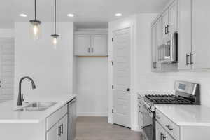 Kitchen featuring appliances with stainless steel finishes, light wood finished floors, recessed lighting, pendant lighting, and light stone counters