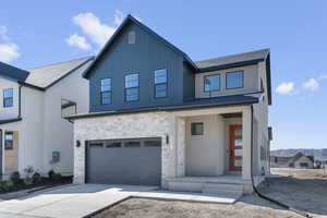 View of front facade with a garage, a porch, driveway, and stone siding