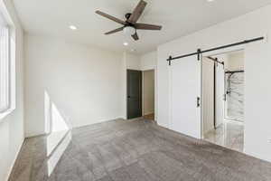 Primary bedroom with light carpet, a barn door, recessed lighting, ceiling fan, and ensuite bathroom