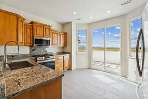 Kitchen with dark stone counters, brown cabinetry, stainless steel appliances, backsplash, and light tile patterned floors