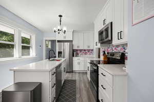 Kitchen featuring appliances with stainless steel finishes, decorative backsplash, white cabinets, dark wood finished floors, and a center island with sink