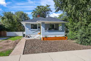 Bungalow-style home featuring a chimney, covered porch, roof with shingles, and brick siding