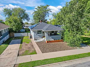 Bungalow-style home featuring roof with shingles, a porch, roof mounted solar panels, a fenced backyard, and brick siding