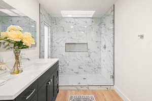 Full bathroom featuring a marble finish shower, vanity, light wood-type flooring, and a skylight