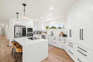Kitchen featuring a center island, a kitchen breakfast bar, pendant lighting, stainless steel appliances, and white cabinets