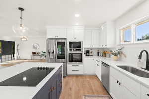 Kitchen with white cabinets, hanging light fixtures, black appliances, light stone counters, and light wood-style floors