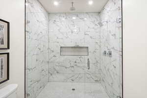 Full bathroom with a marble finish shower and toilet