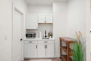 Bar with white cabinetry, stainless steel microwave, and light wood-style floors