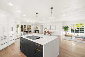 Kitchen with open floor plan, pendant lighting, light wood finished floors, dark cabinetry, and white cabinets