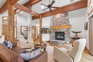 Living area featuring a towering ceiling, wood finished floors, a stone fireplace, beam ceiling, and ceiling fan