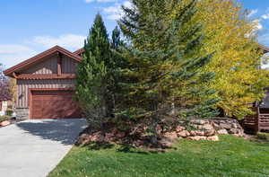 View of front of property featuring driveway, stone siding, board and batten siding, and a front yard