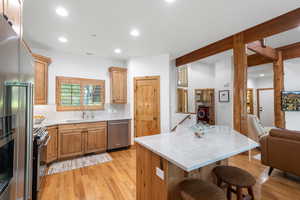 Kitchen with appliances with stainless steel finishes, a breakfast bar, tasteful backsplash, light wood-style floors, and light stone countertops
