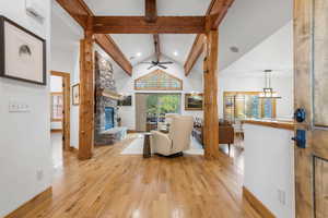 Living room with high vaulted ceiling, light wood finished floors, beam ceiling, a stone fireplace, and a ceiling fan
