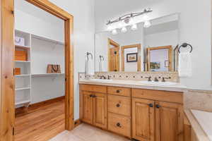 Bathroom featuring backsplash, double vanity, a spacious closet, light wood-style flooring, and a bath