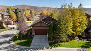 View of front of property with stone siding, a mountain view, concrete driveway, a garage, and a chimney