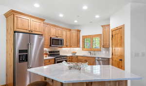 Kitchen with stainless steel appliances, tasteful backsplash, light stone countertops, recessed lighting, and light brown cabinets