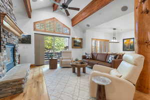 Living room featuring a fireplace, wood-type flooring, high vaulted ceiling, beam ceiling, and a ceiling fan