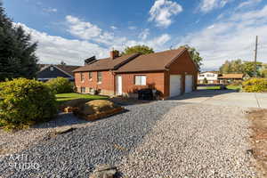 View of side of home with brick siding, concrete driveway, a chimney, a garage, and a shingled roof