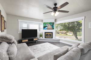 Living area with a textured ceiling, dark wood-style flooring, a glass covered fireplace, and ceiling fan