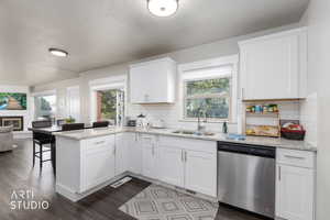 Kitchen with stainless steel dishwasher, a peninsula, white cabinetry, a glass covered fireplace, and light stone countertops